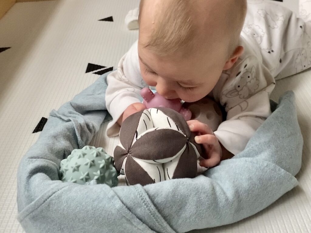 A baby lies on his tummy with a blanket in a U shape. The blanket keeps balls from rolling away.
