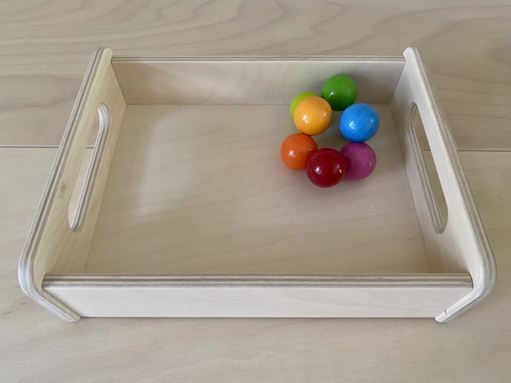 A wooden tray containing colorful grasping balls for baby