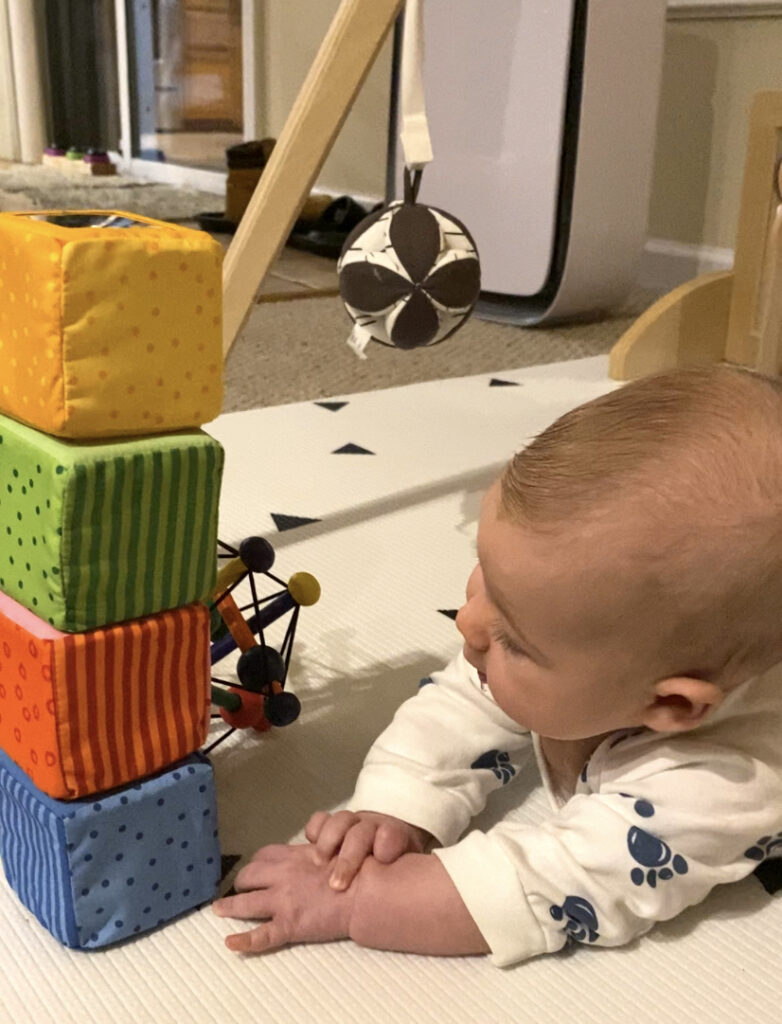 Baby on tummy looking at a stack of 4 colorful blocks